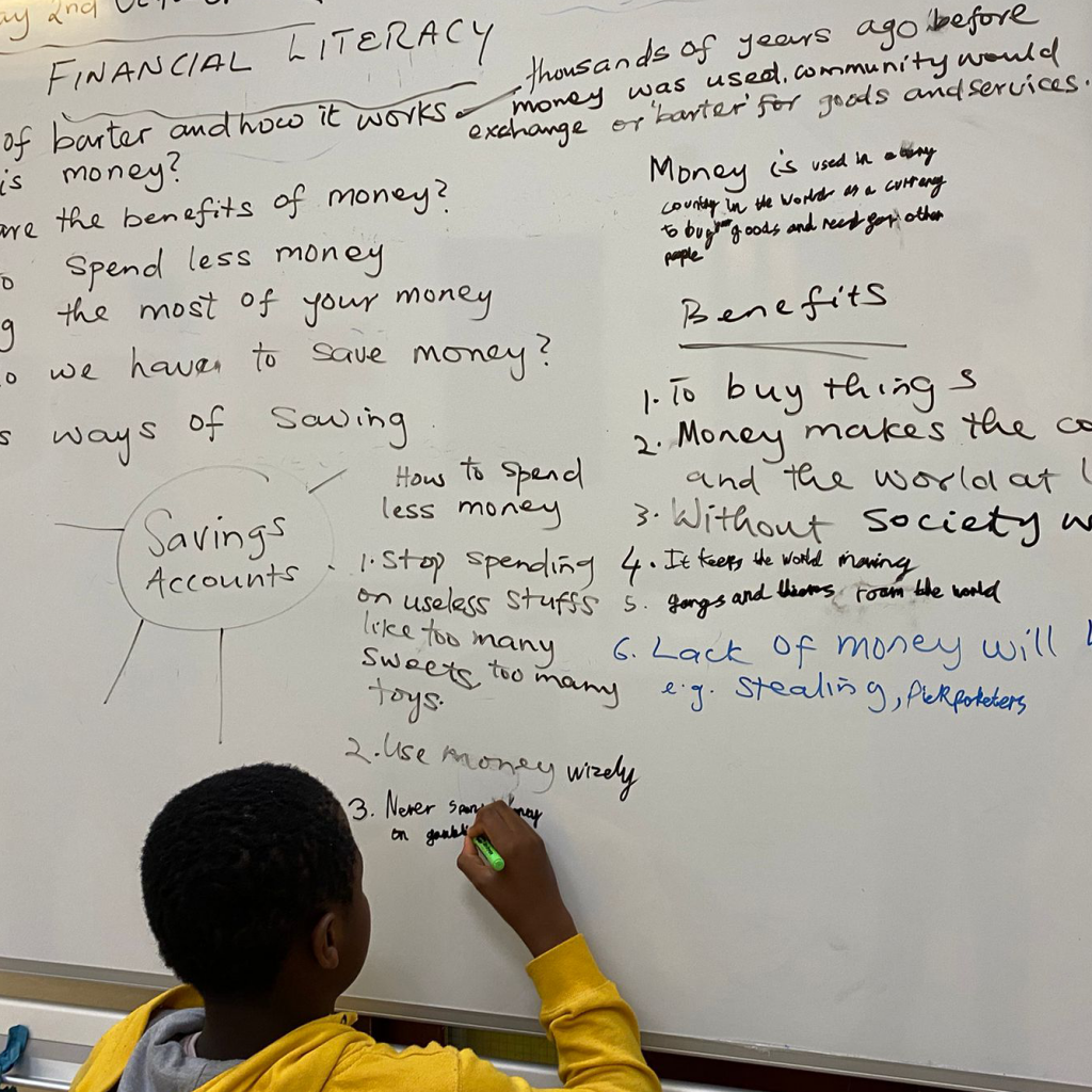 A child writing on a white board where other children have written things about financial education