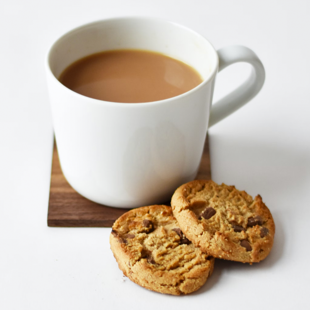 a cup of tea in a white mug with two chocolate chip biscuits next to it