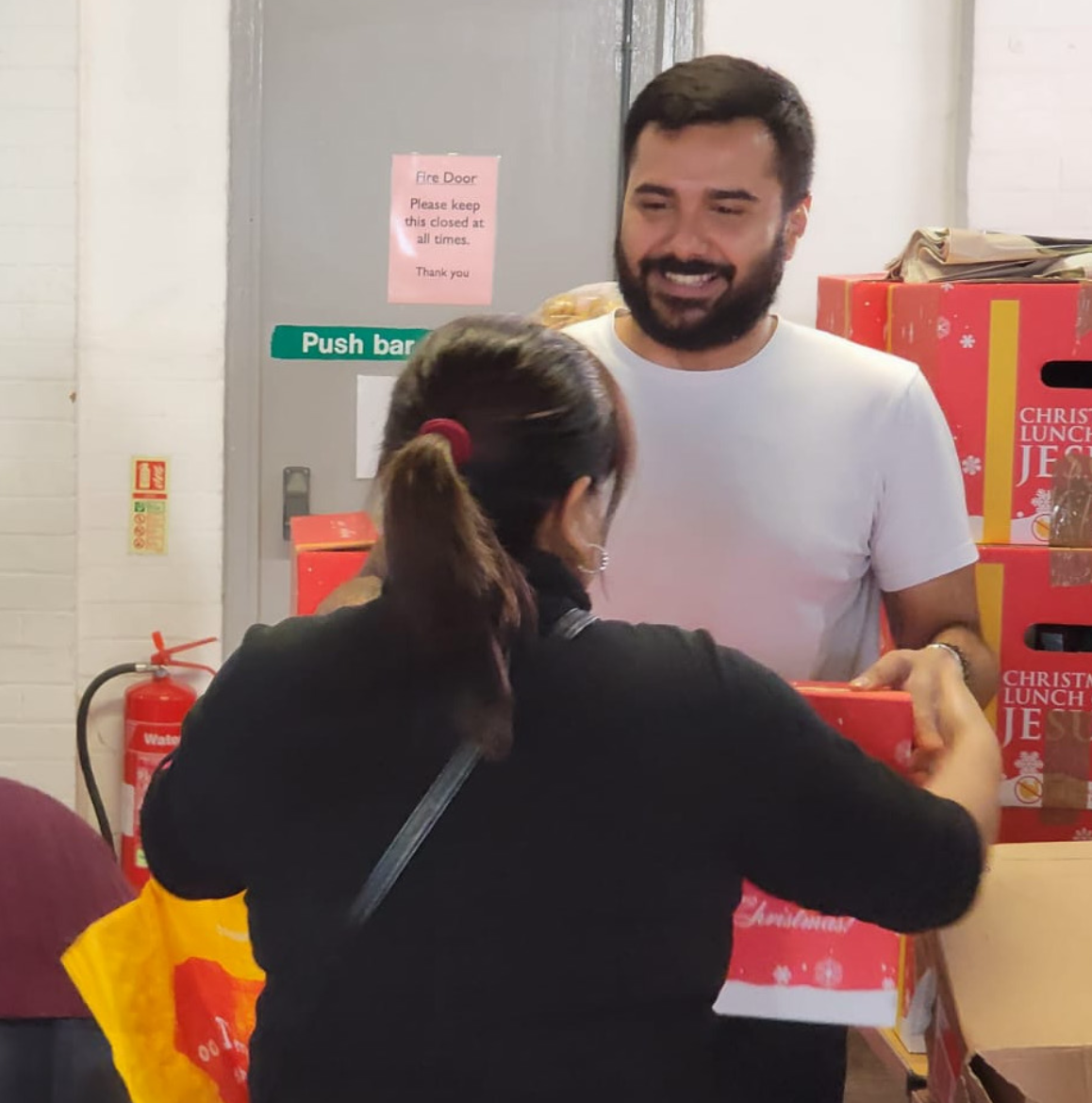 A man smiles whilst handing a food parcel to a woman