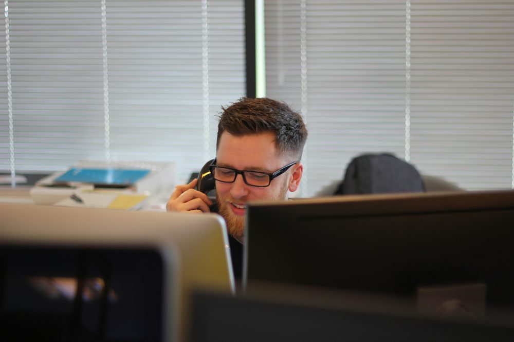 A man sitting at a computer on the phone smiling
